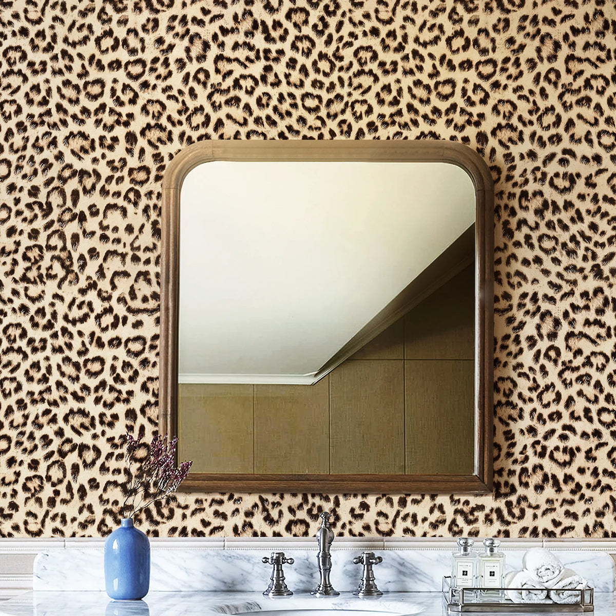 A mirror framed in wood hangs on a leopard print wall, with a vase of purple flowers and marble countertop below.