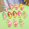A collection of resin mermaid princess charms in various pink, yellow, and green colors arranged on a light green surface.