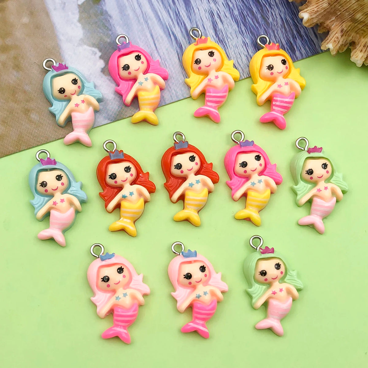 A collection of resin mermaid princess charms in various pink, yellow, and green colors arranged on a light green surface.