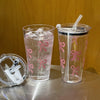 A clear plastic cup filled with water and ice, decorated with pink bow patterns, sits next to a similar cup.