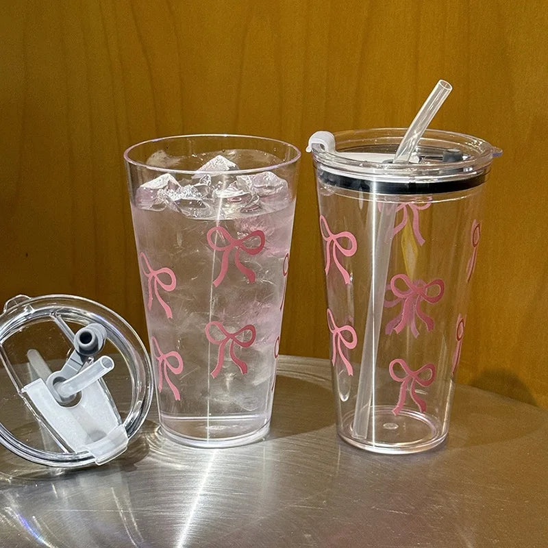 A clear plastic cup filled with water and ice, decorated with pink bow patterns, sits next to a similar cup.