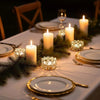 A close-up of a dining table setting with candles and greenery, featuring a crystal tealight candle holder.