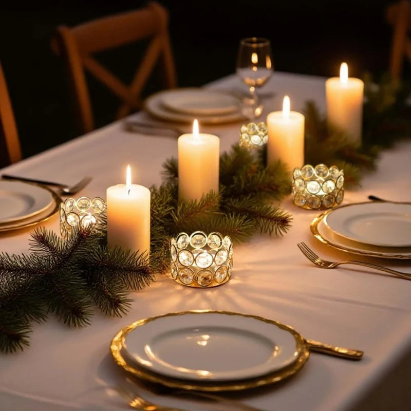 A close-up of a dining table setting with candles and greenery, featuring a crystal tealight candle holder.