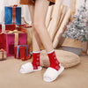 A pair of red Christmas socks with reindeer and tree patterns are shown on a person's foot.