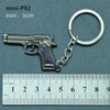 A silver miniature replica of a handgun is attached to a metal keyring, measured against a ruler.