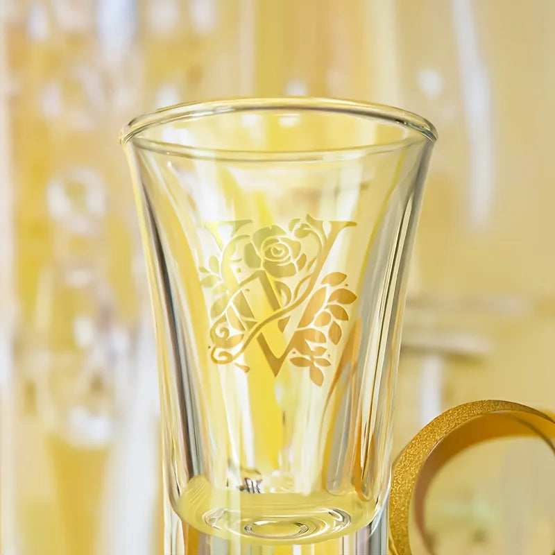 A clear glass object with a floral alphabet design etched onto it, set against a yellow background.