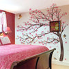 A bedroom featuring a pink cherry blossom tree wall sticker above a bed.