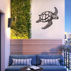A dark metal sea turtle wall art piece is displayed on a white wall above a wooden panel and a blue sofa.