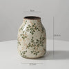 A rustic ceramic milk pitcher with a pale cream glaze and green pastoral floral design.