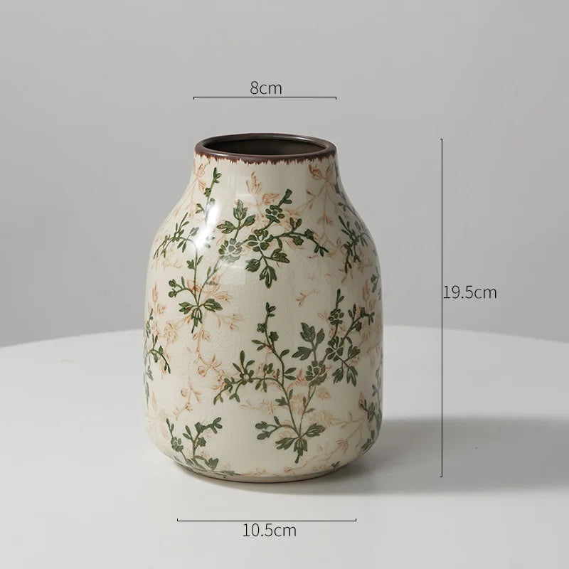 A rustic ceramic milk pitcher with a pale cream glaze and green pastoral floral design.
