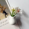 A white ceramic vase holding artificial white and pink flowers placed on a light-colored book.