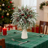 A festive centerpiece of artificial pine branches decorated with red berries and pine cones on a green tablecloth.
