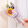 A bouquet of handmade crochet flowers in yellow and purple velvet blooms wrapped in clear cellophane for gifting