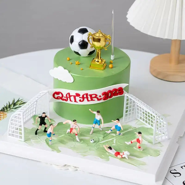 A green birthday cake with a golden trophy and soccer ball topper, surrounded by a white soccer field design.