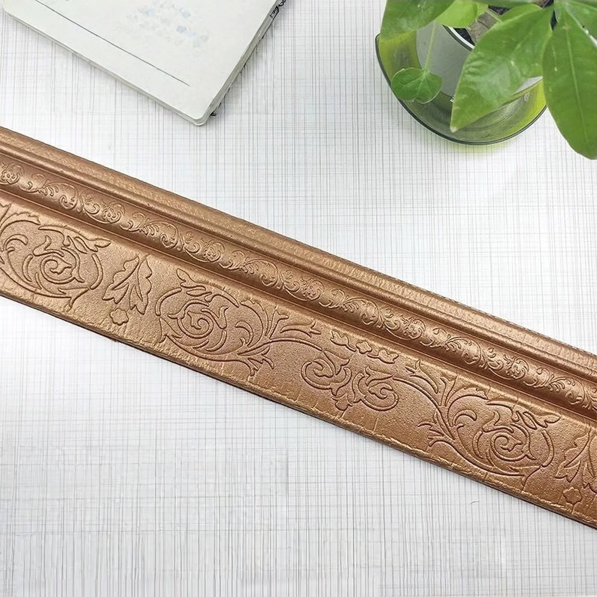 A close-up of a gold-colored self-adhesive 3D wall trim line featuring an ornate floral pattern.