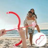 A couple is using a red Cupid heart bow and arrow prop on a beach with the ocean in the background.