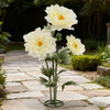 Large artificial silk yellow poppy flower displayed on a green stand in a garden setting.