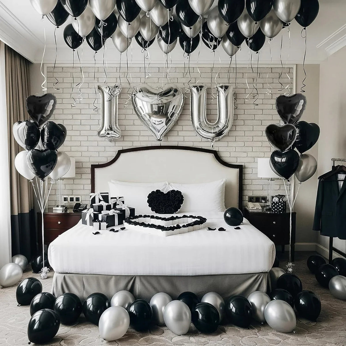 Un lit décoré de ballons en forme de cœur argentés et noirs, face à un mur de briques blanches.