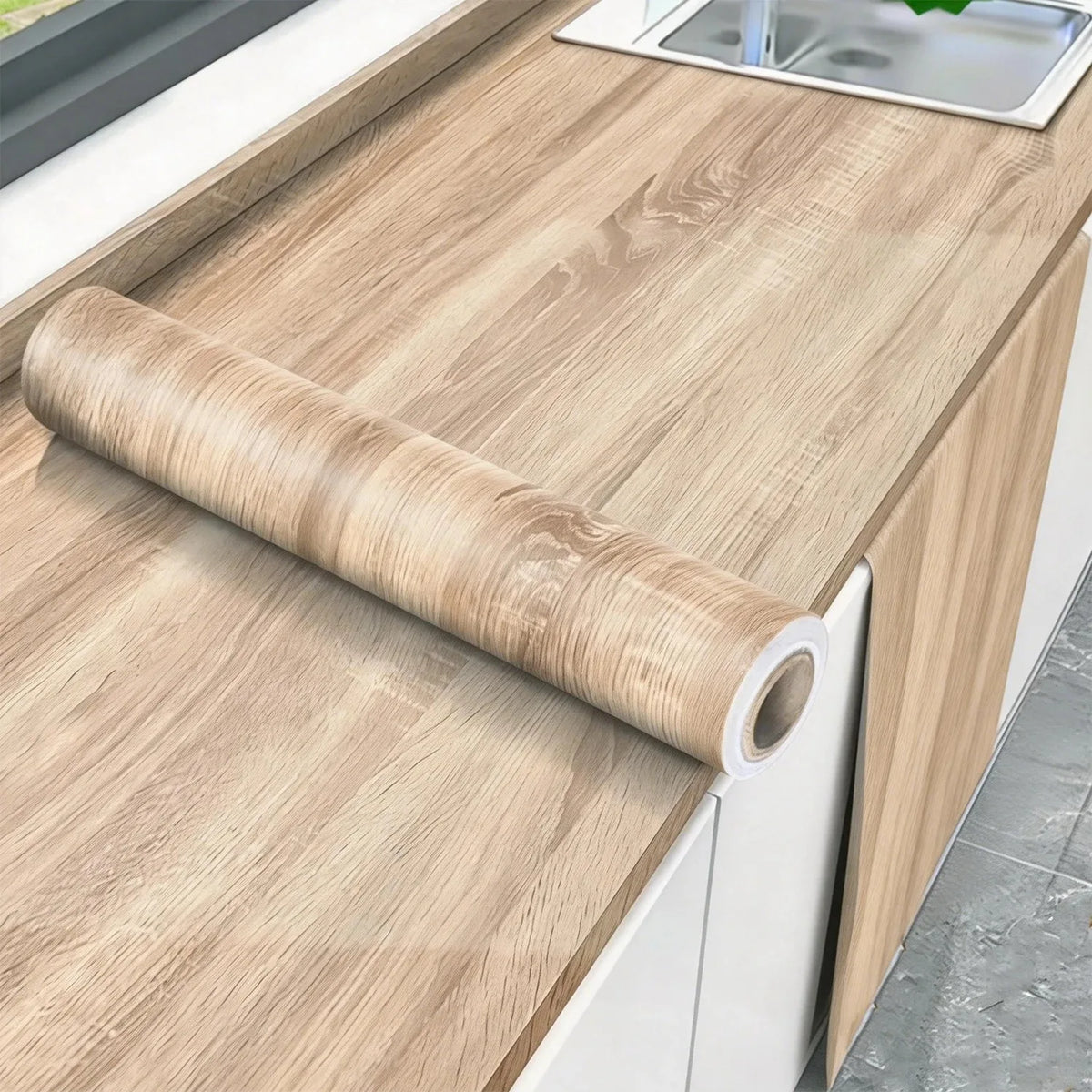 A roll of self-adhesive wood grain wallpaper is placed on a light wood countertop next to a sink.
