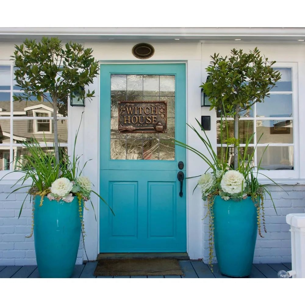 A turquoise door with a vintage witch house metal sign and floral arrangements on a porch.