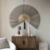 A large, fan-shaped wall decor made of woven bamboo strands with a dark tassel hanging on a light gray wall.