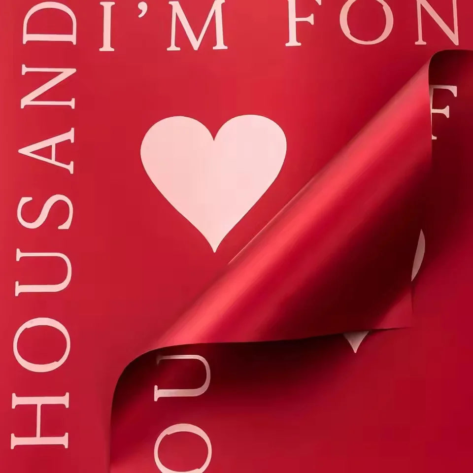 A close-up of red wrapping paper with white text and a pink heart design.