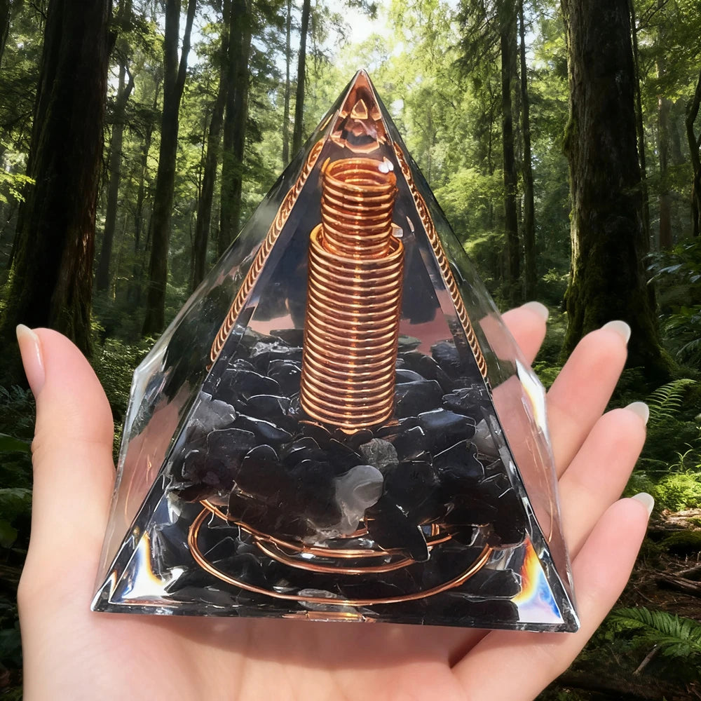 Handmade resin orgonite pyramid featuring natural obsidian and a copper coil set against a forest background.