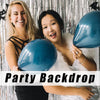 Two women smiling in front of a silver metallic foil fringe curtain backdrop for a party backdrop.