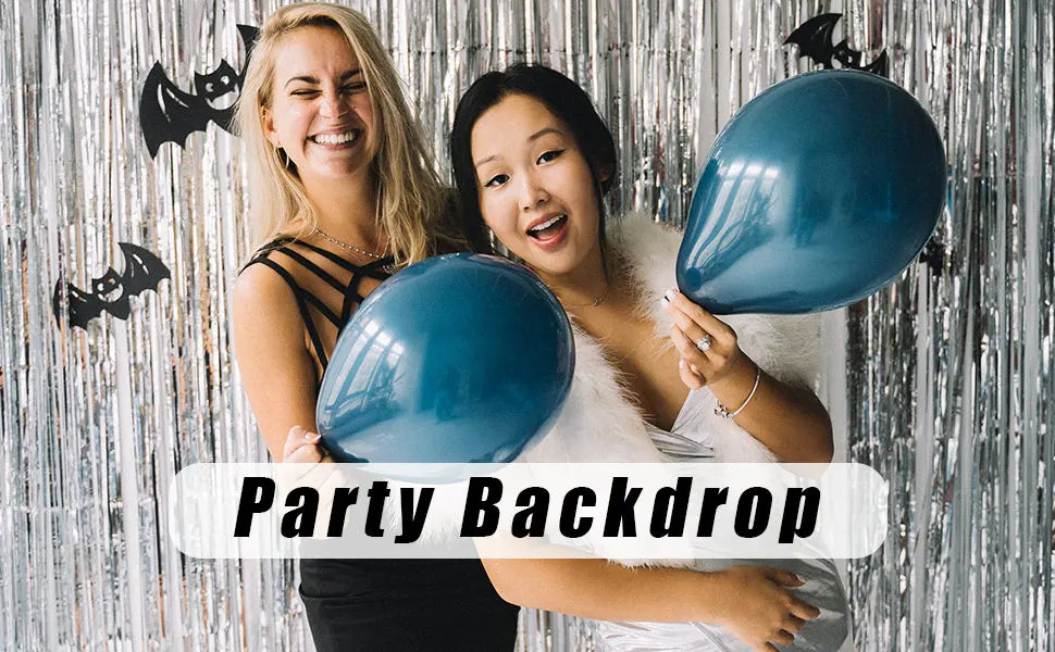 Two women smiling in front of a silver metallic foil fringe curtain backdrop for a party backdrop.