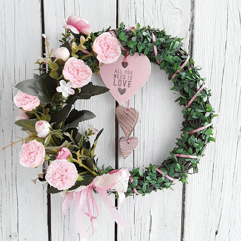 A wreath made of green foliage and pink silk peony artificial flowers with a heart tag