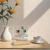 An acrylic desk sign with a positive message about self-worth sits on a wooden surface next to a white cup and a plant.
