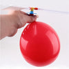 A hand is holding the propeller of a red balloon helicopter toy against a white background.