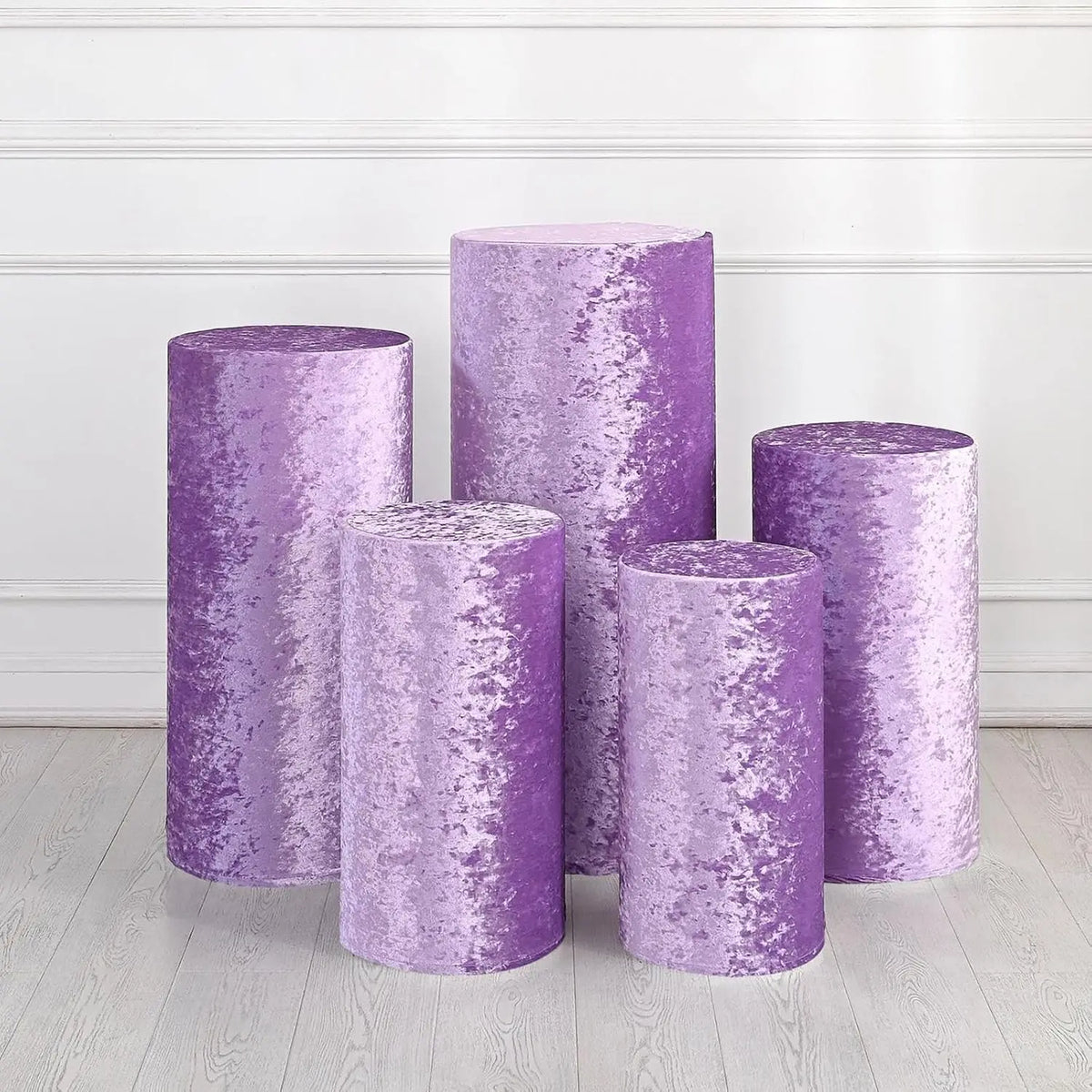 A collection of purple spandex cylinder stands used for weddings and events, displayed against a white wall.