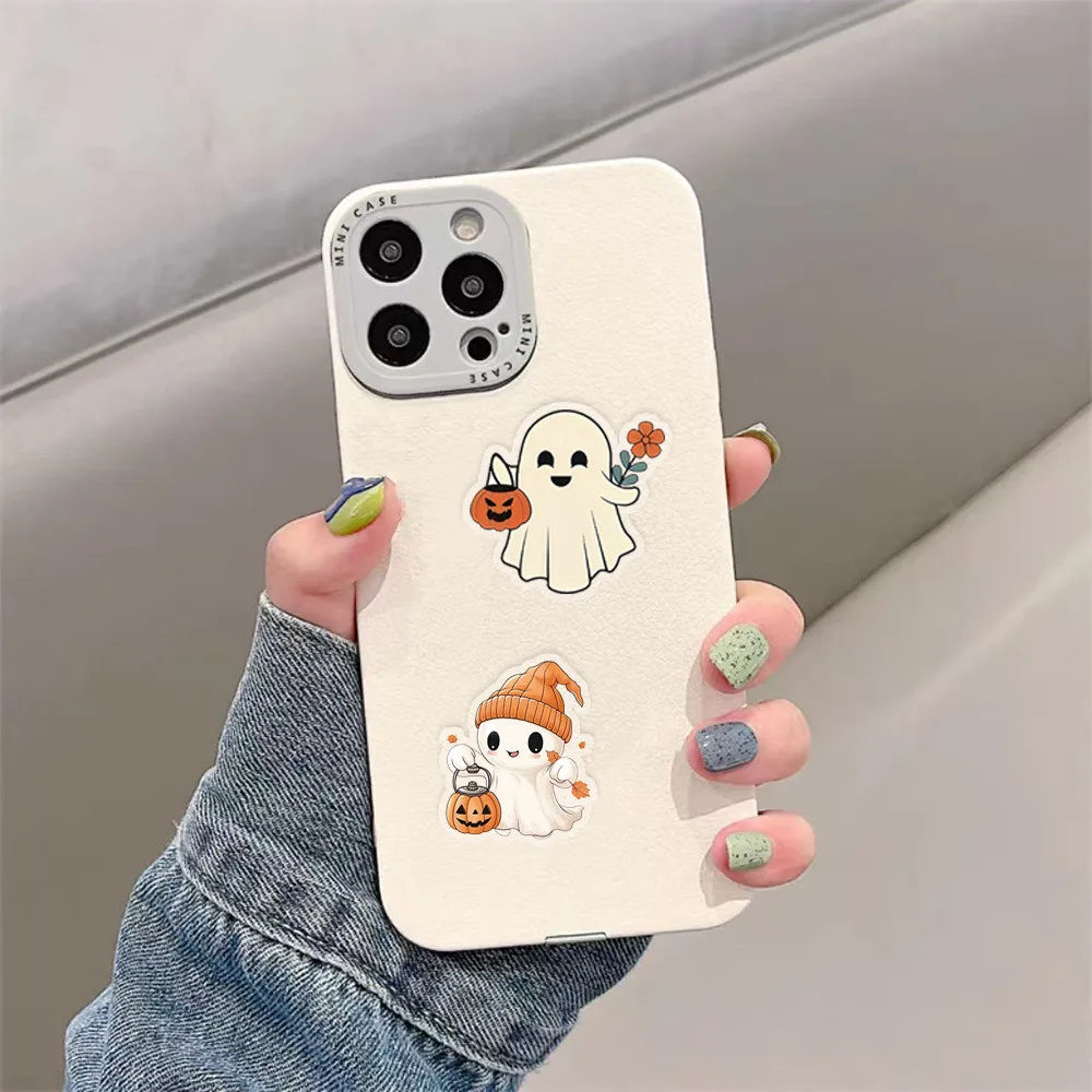 A hand holds a white phone case decorated with transparent DIY stickers featuring a ghost and pumpkins.