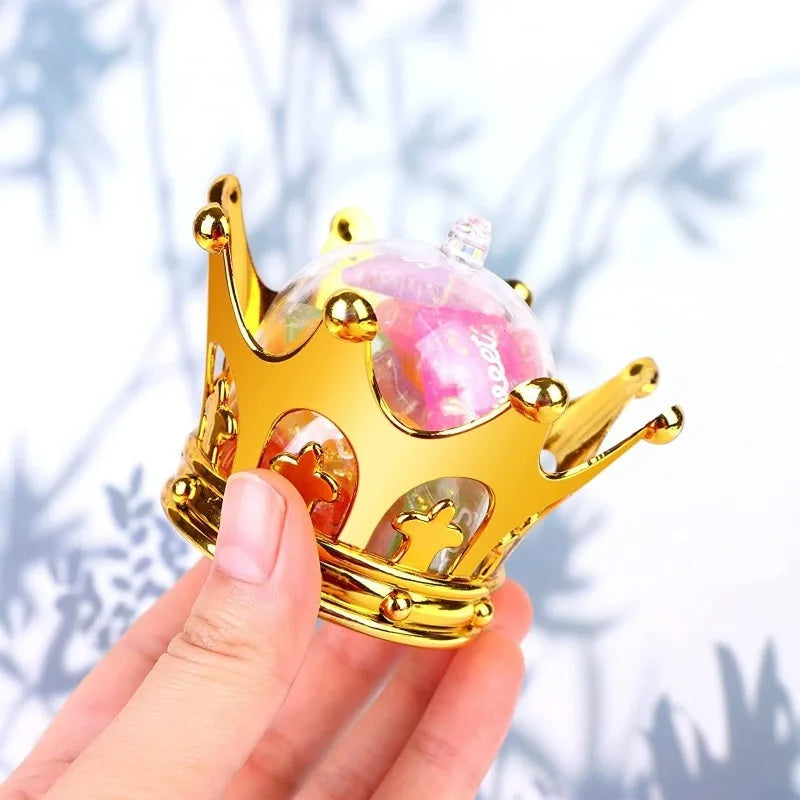 A hand holds a gold crown with pink and clear candy boxes, set of twelve.