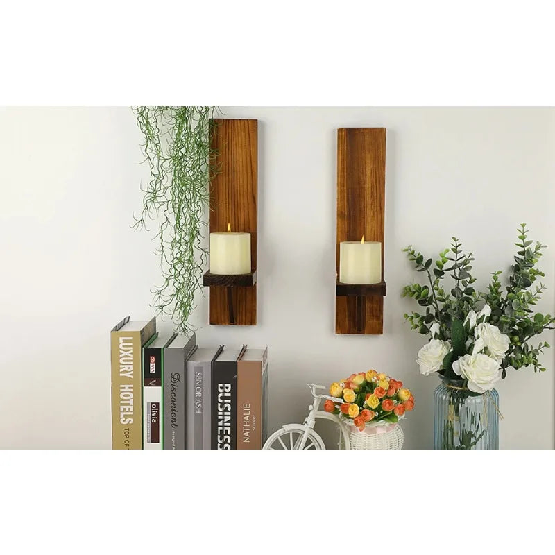 Vintage wooden wall candle holders with green foliage and a stack of books on a white wall.