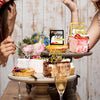 A tiered display of birthday cakes and mirrored gold acrylic cake toppers being held by two people.