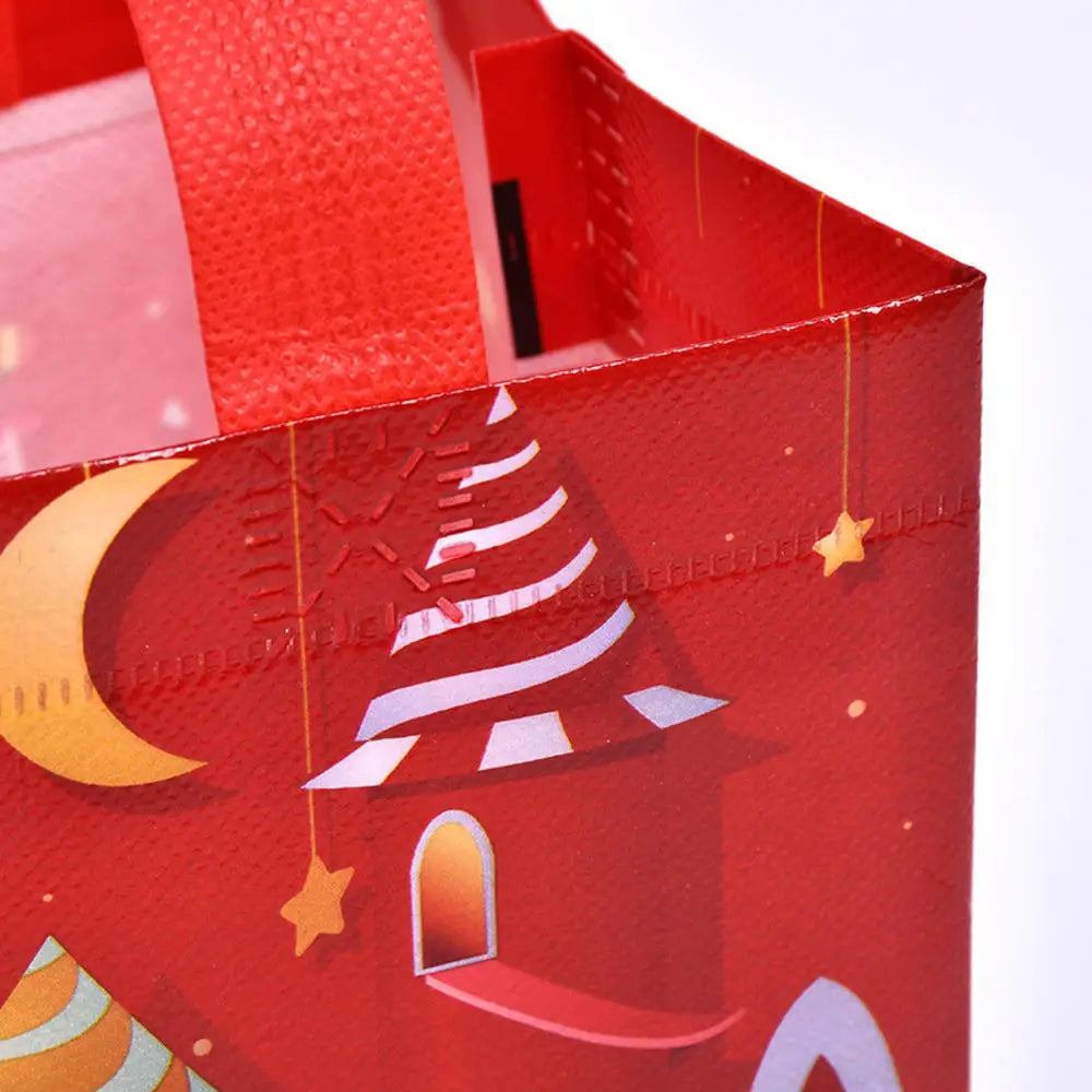 A close-up view of a red non-woven gift tote bag featuring white and gold holiday prints like a Christmas tree and stars.