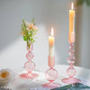 Three pink wavy glass taper candle holders with lit candles on a white surface.