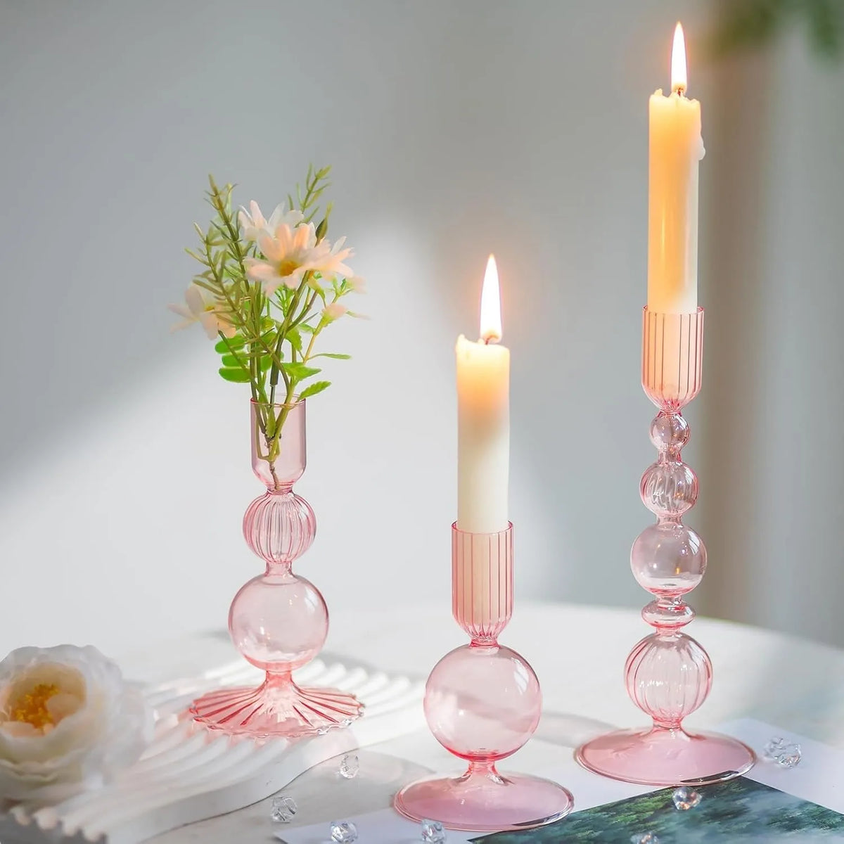 Three pink wavy glass taper candle holders with lit candles on a white surface.