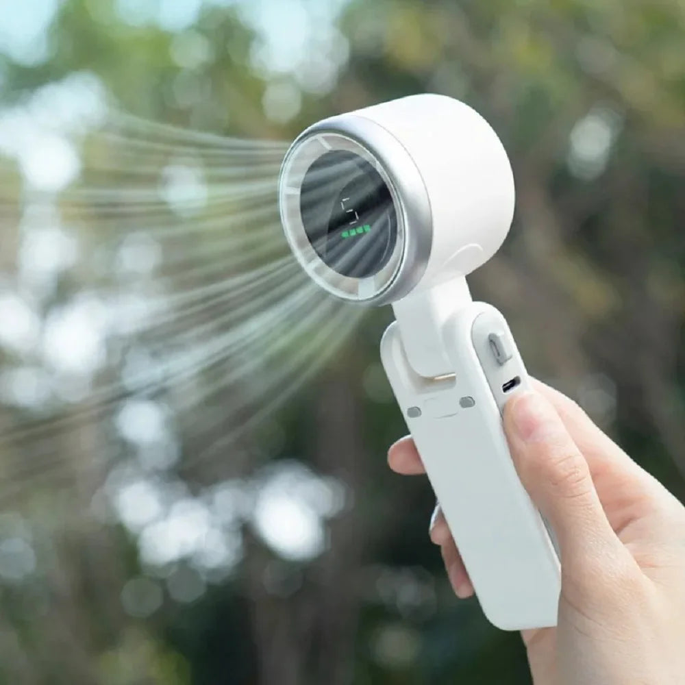 A hand holds a white foldable mini handheld fan with a light emitting nozzle, directing air into the distance.