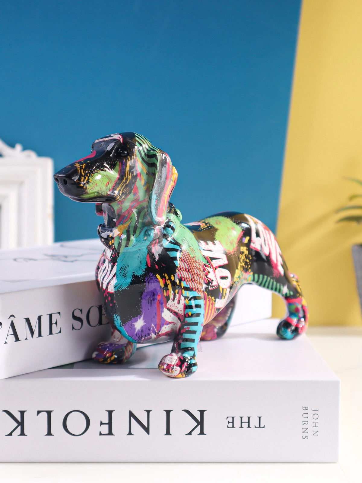 A colorful resin figurine of a dachshund dog standing on a white book.
