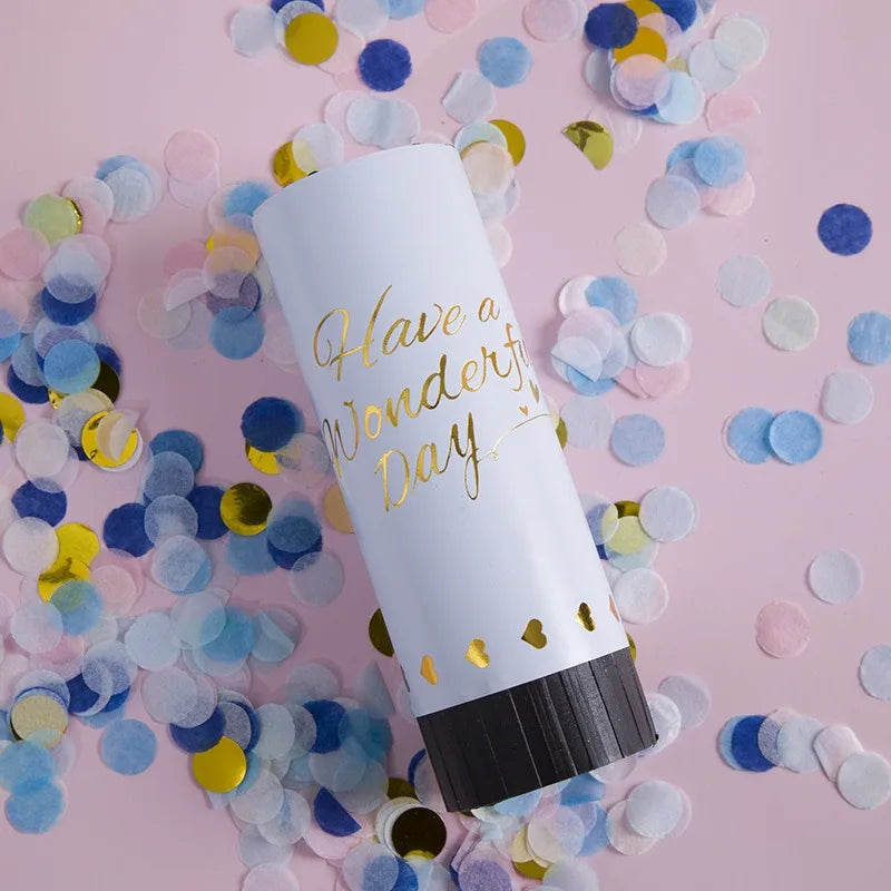 A white tube of Hand Twist Confetti Cannons lying on pink surface surrounded by scattered confetti.