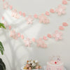 Pink cherry blossom paper flag banner strung across a white wall with soft shadows.