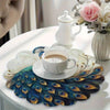 A set of four peacock feather placemats and a white teapot displayed on a dining table.