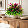 A potted artificial Dracaena Boston Fern with vibrant pink and green leaves sits on a wooden cabinet top.