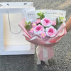A bouquet of handmade crochet flowers in pink and white, wrapped in sheer paper, displayed next to its packaging.