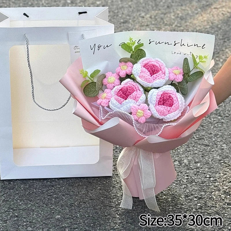 A bouquet of handmade crochet flowers in pink and white, wrapped in sheer paper, displayed next to its packaging.