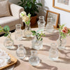 A collection of diamond faceted glass bud vases and a floral arrangement on a wooden table.