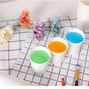 A collection of disposable paper cups in various colors, including orange, green, and blue, arranged on a checkered surface.